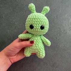 a hand holding a small green crocheted stuffed animal with black eyes and ears