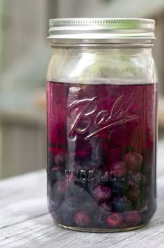 a jar filled with blueberries and raspberries sitting on top of a wooden table