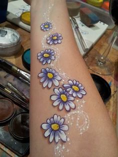 a woman's arm with flowers painted on it and some paintbrushes in the background