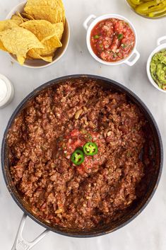 a pan filled with chili and tortilla chips next to bowls of guacamole