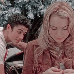 a man and woman looking at something on their cell phones in front of snow covered trees