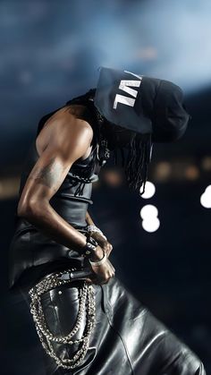 a man with a hat and chains on his head standing in front of a dark background