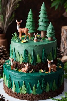 a green cake with deer and trees on it's side, surrounded by pine cones