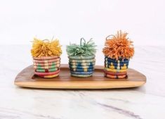 three small baskets are sitting on a wooden platter, each with different colored yarns