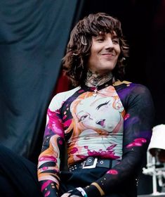 a man with long hair and tattoos on his body sitting in front of a microphone