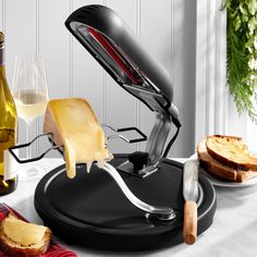 a cheese slicer is being used to cut into slices on a table with wine and bread