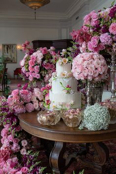 a table topped with a white cake covered in pink flowers next to tall vases