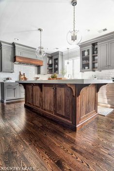 a large kitchen with wooden flooring and gray cabinetry, along with an island in the middle