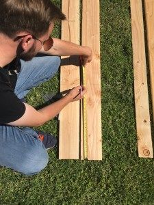 a man sitting on the ground working on wood planks with a cell phone in his hand