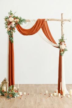 an orange and white wedding arch decorated with flowers, greenery and candles on a wooden floor