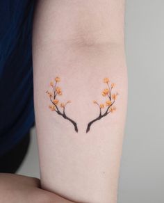 a woman's arm with two branches that have orange flowers on them and one branch has black leaves