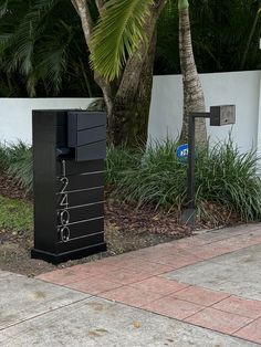 there is a black box on the sidewalk next to a palm tree and some bushes