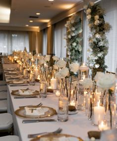 a long table is set with candles and flowers in glass vases, plates and silverware