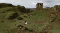 an aerial view of a bride and groom walking through the green hills on their wedding day