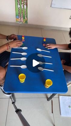 two people sitting at a blue table with spoons and cups on it in front of them