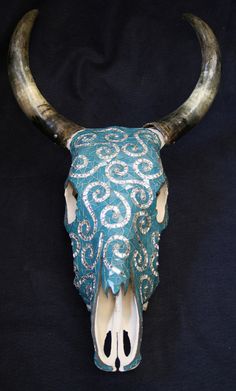 a bull's skull decorated with blue and white beaded fabric on a black background