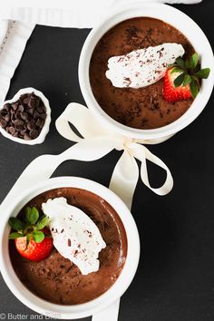 two bowls of chocolate pudding with whipped cream and strawberries on the side, sitting on a black surface