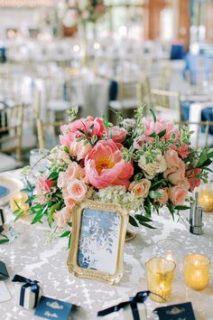 a table topped with a vase filled with pink flowers and greenery next to candles