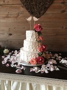 a white wedding cake with pink flowers on the table next to it and a wooden wall behind it