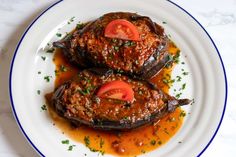 two stuffed eggplant halves with tomato sauce on a white and blue rimmed plate