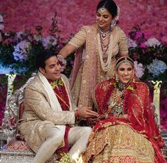 a bride and groom sitting on a bench in front of a flowered wall with candles