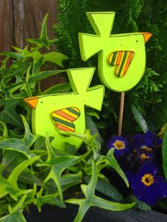 two wooden birds sitting on top of green plants