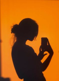 the silhouette of a woman holding a camera in front of an orange wall with light coming through it