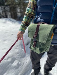 a man walking his dog in the snow with a bag on it's back