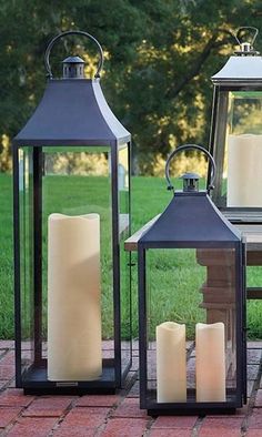 three lanterns with lit candles sitting on a brick walkway in front of a grassy area