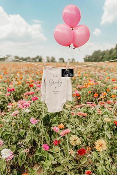 some pink and white balloons are hanging in the air over an open field full of flowers