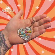 a hand holding a heart shaped pin with buttons on it's thumb and an orange background