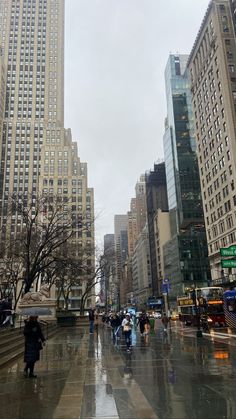 people walking in the rain on a city street with tall buildings behind them and one person holding an umbrella