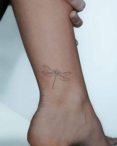 a woman's foot with a small dragonfly tattoo on her left side leg