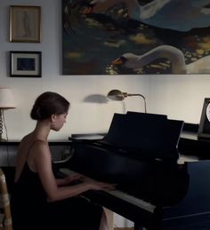 a woman sitting at a black piano in front of a clock and swan painting on the wall