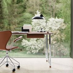 a desk with a chair, lamp and laptop on it in front of a window