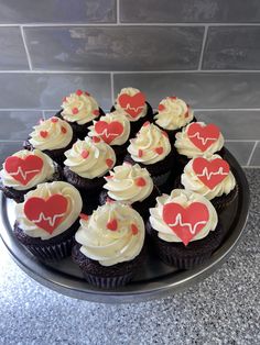 cupcakes with white frosting and red heart decorations on a black platter