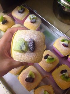 a person is holding up small pastries with kiwis and grapes on them