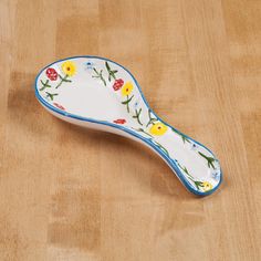 a ceramic spoon sitting on top of a wooden table next to a bowl with flowers painted on it