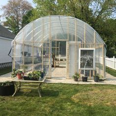 a small greenhouse in the middle of a yard with potted plants and a table