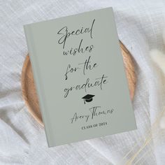 an open book on a plate with some flowers in front of it that says special wishes for the graduate