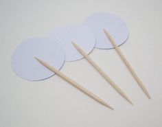 four white paper circles with wooden sticks sticking out of them on a white table top