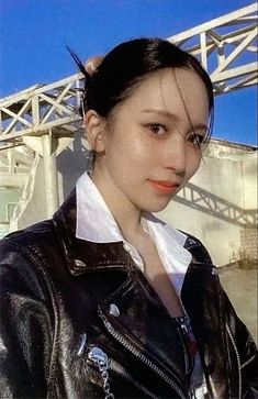 a woman in a black leather jacket and white shirt is posing with her hair pulled back