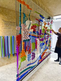 a woman standing next to a wall covered in lots of different colored beads and wires