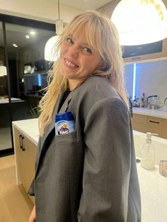 a woman standing in a kitchen wearing a gray blazer and smiling at the camera