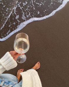 a person sitting on the beach with a glass of wine in their hand and water coming out of the ocean behind them