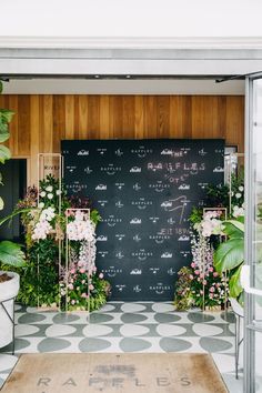 the entrance to an event with flowers and greenery in front of a blackboard