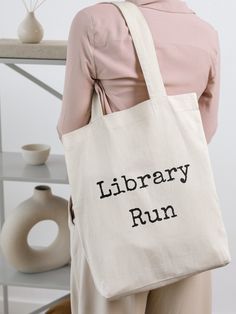 Introducing the stylish and practical Library Run Tote Bag, designed to cater to all your literary adventures. Whether you're heading to the local library, bookstore, or simply out and about, this versatile tote bag is a must-have accessory for book lovers.   -  100% cotton canvas -  Heavy fabric (12 oz/yd² (406.9 g/m -  Dimensions:  15" x 16" and 20" handles Bookish School Bags With Letter Print, Bookish Tote Bag With Letter Print, Literary Style Letter Print Bag, Library Book Bag, Library Tote Bag, Library Tote, Library Bag, Book Bags, Local Library