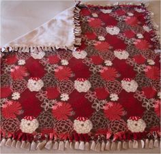 a red and brown blanket laying on top of a white tablecloth with fringes