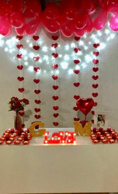 a table topped with lots of red heart shaped balloons and candles next to a sign that says love