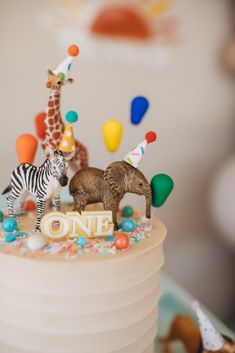 a small birthday cake with animals and balloons on the top, as well as a one year sign